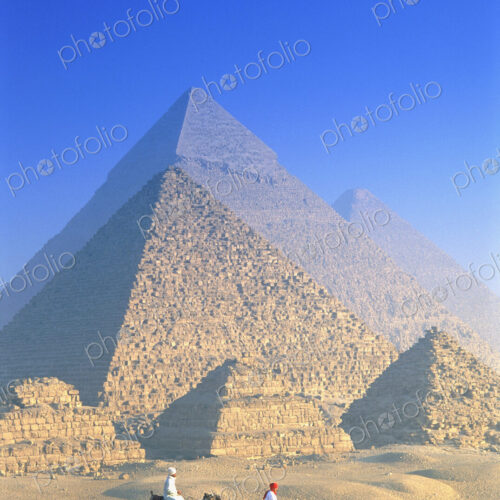 Two people on camels in front of Egyptian pyramids.