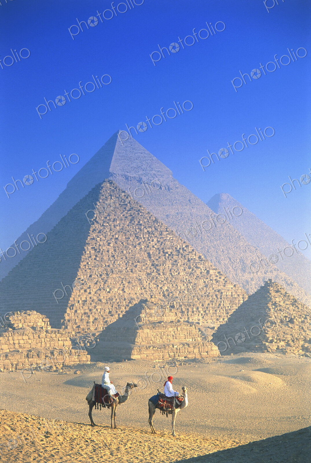 Two people on camels in front of Egyptian pyramids.