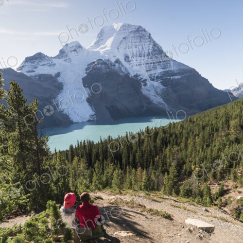 Two people resting by a hiking path, view of Mount Robson and the Rockies.