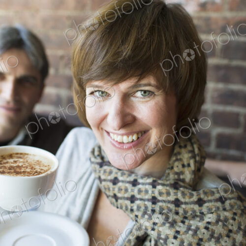 Two people sitting in a coffee shop. A man and woman, holding white china cups of…