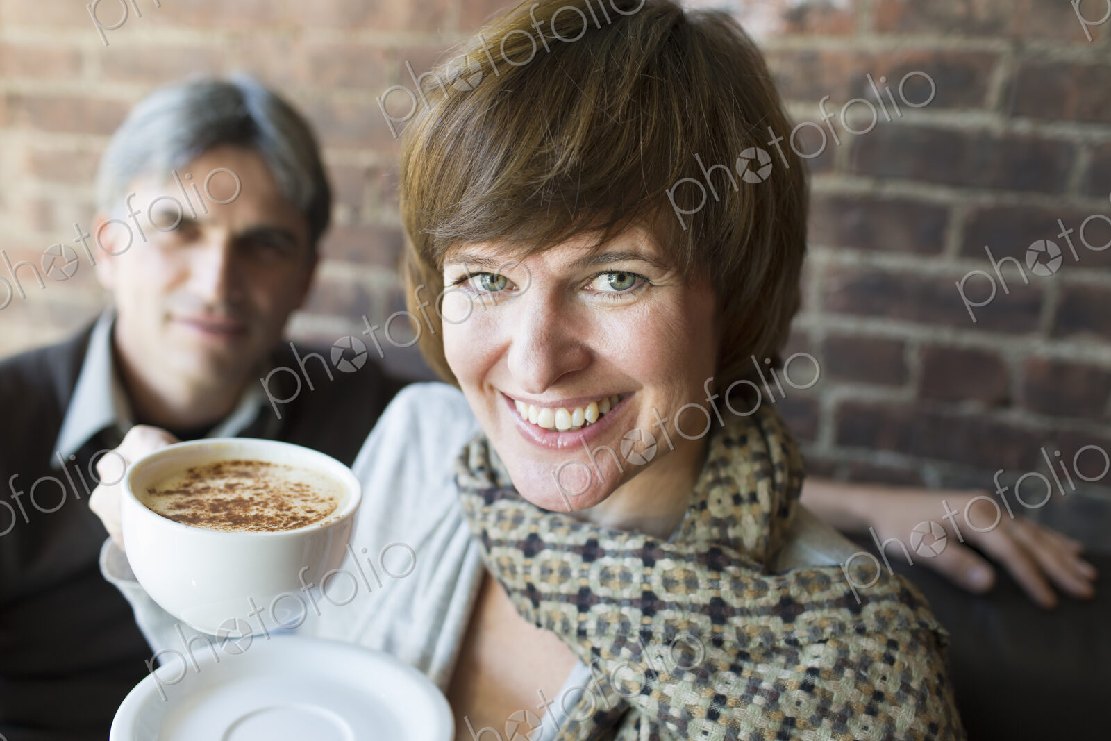Two people sitting in a coffee shop. A man and woman, holding white china cups of…