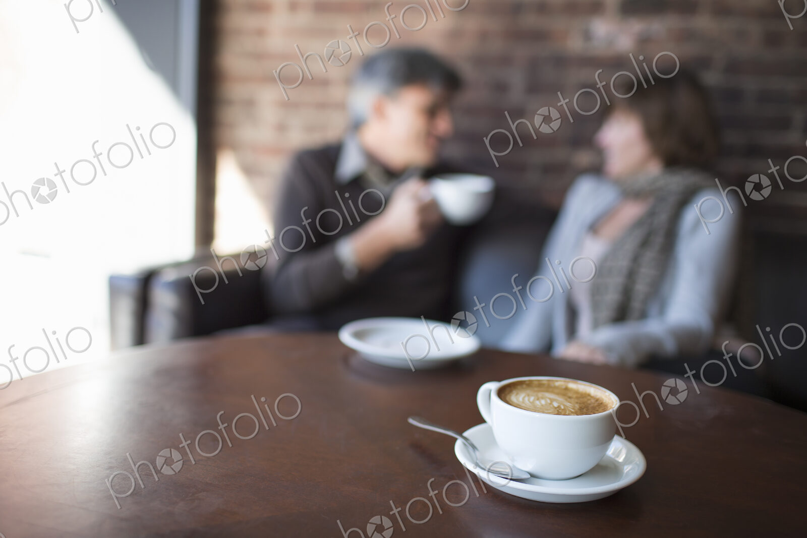 Two people sitting in a coffee shop. A man holding a white china of and drinking.…