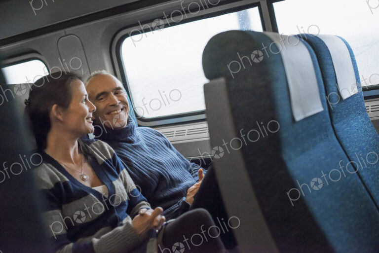 Two people sitting in a railway carriage, smiling. Taking a train journey.