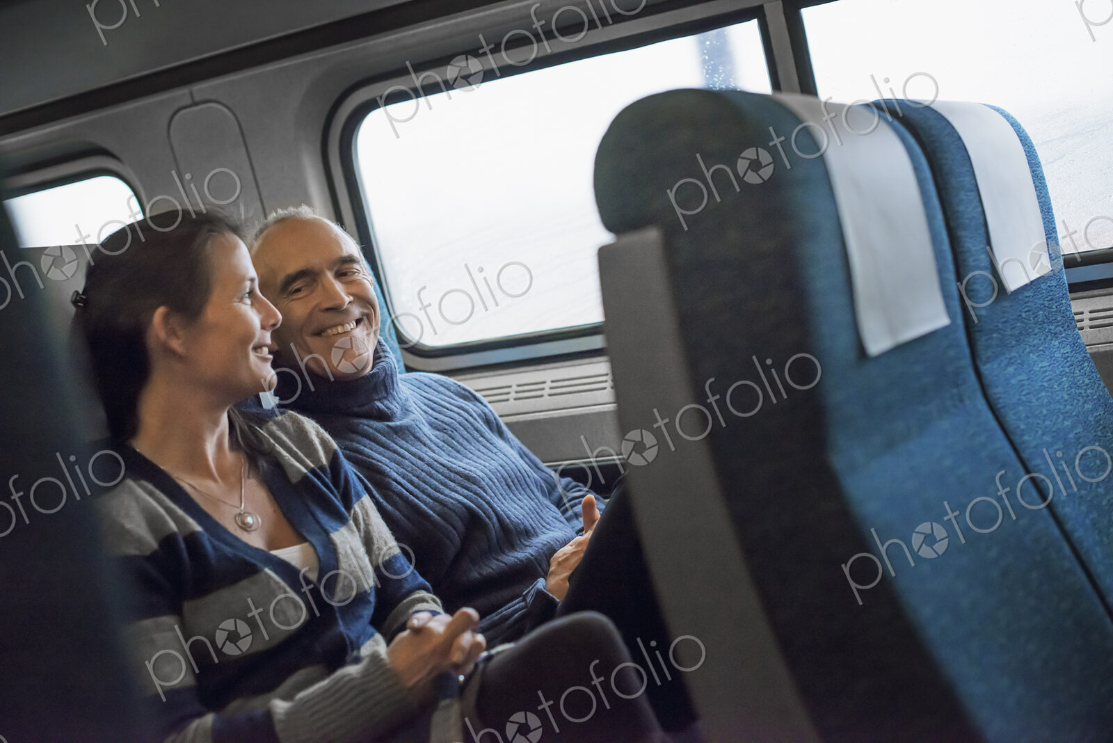 Two people sitting in a railway carriage, smiling. Taking a train journey.