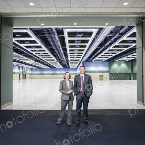 Two people standing in the entrance to a large convention center arena. Two people standing in the entrance to a large convention center arena.