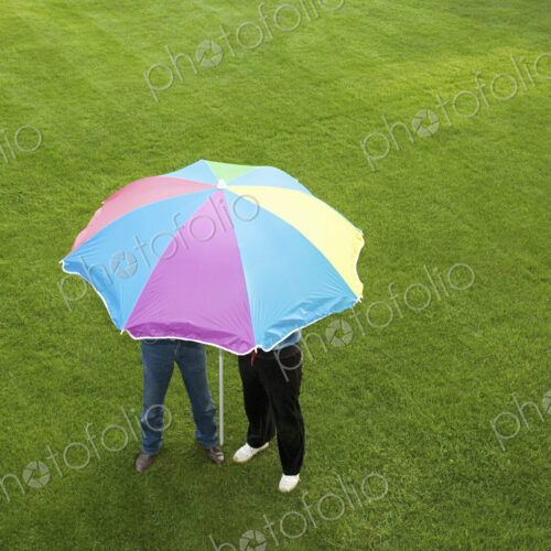 Two people under a striped umbrella on a lawn.