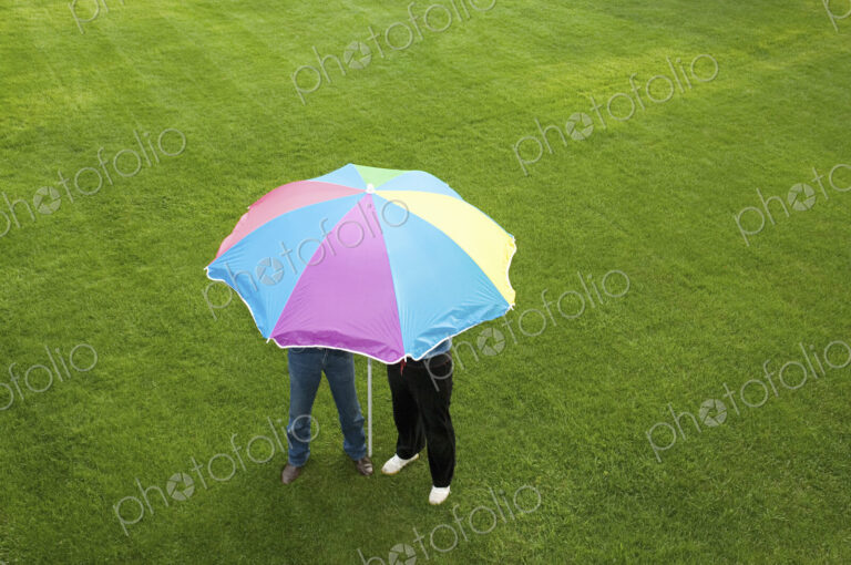 Two people under a striped umbrella on a lawn.