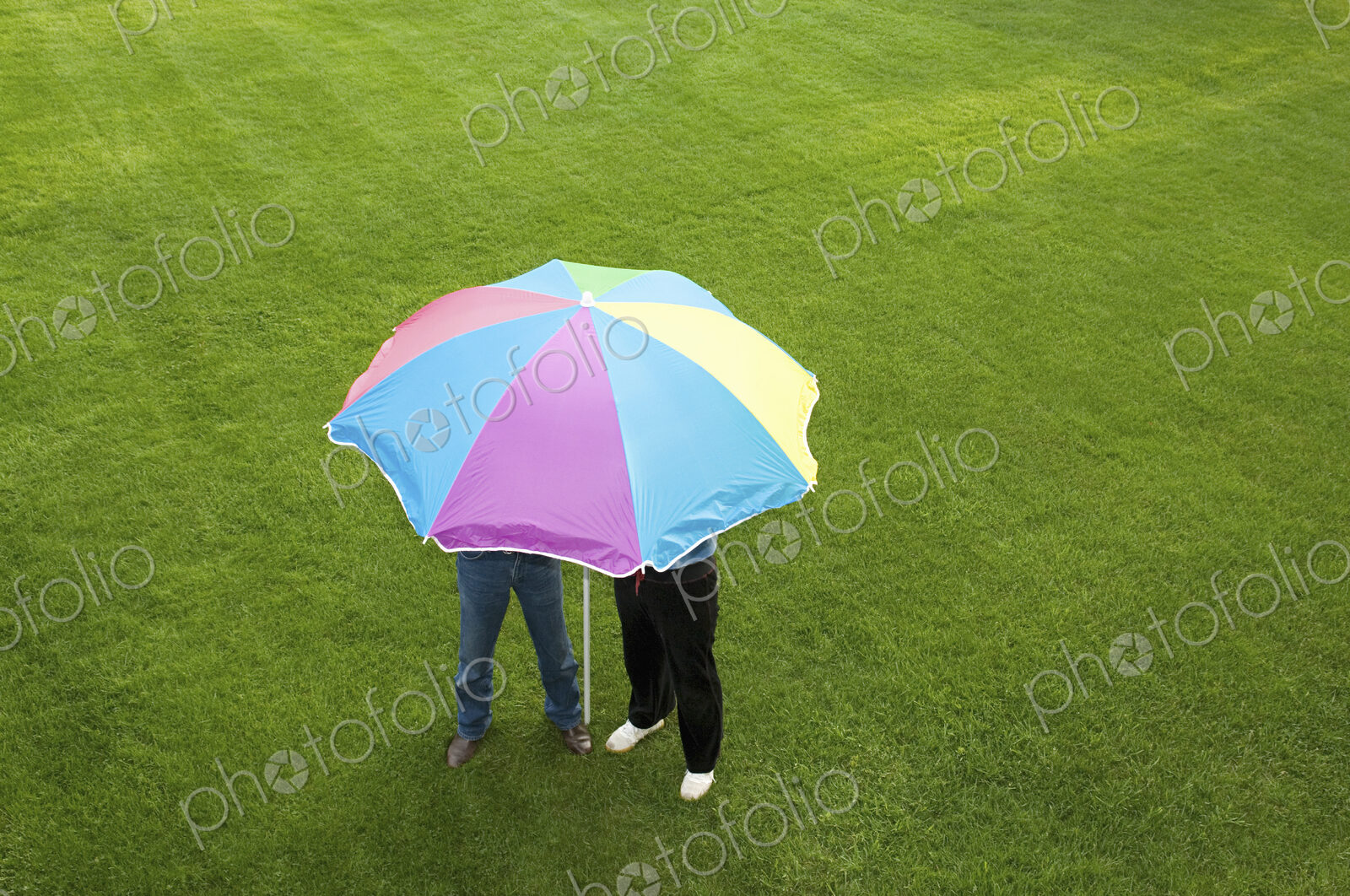 Two people under a striped umbrella on a lawn.