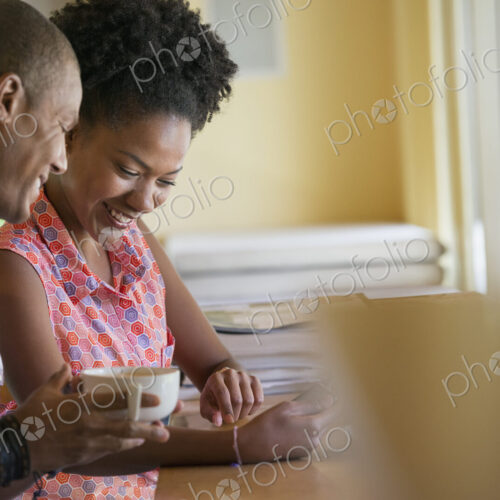 Two people using a digital tablet, seated close together at a cafe. Coffee cups. Two people using a digital tablet, seated close together at a cafe. Coffee cups.