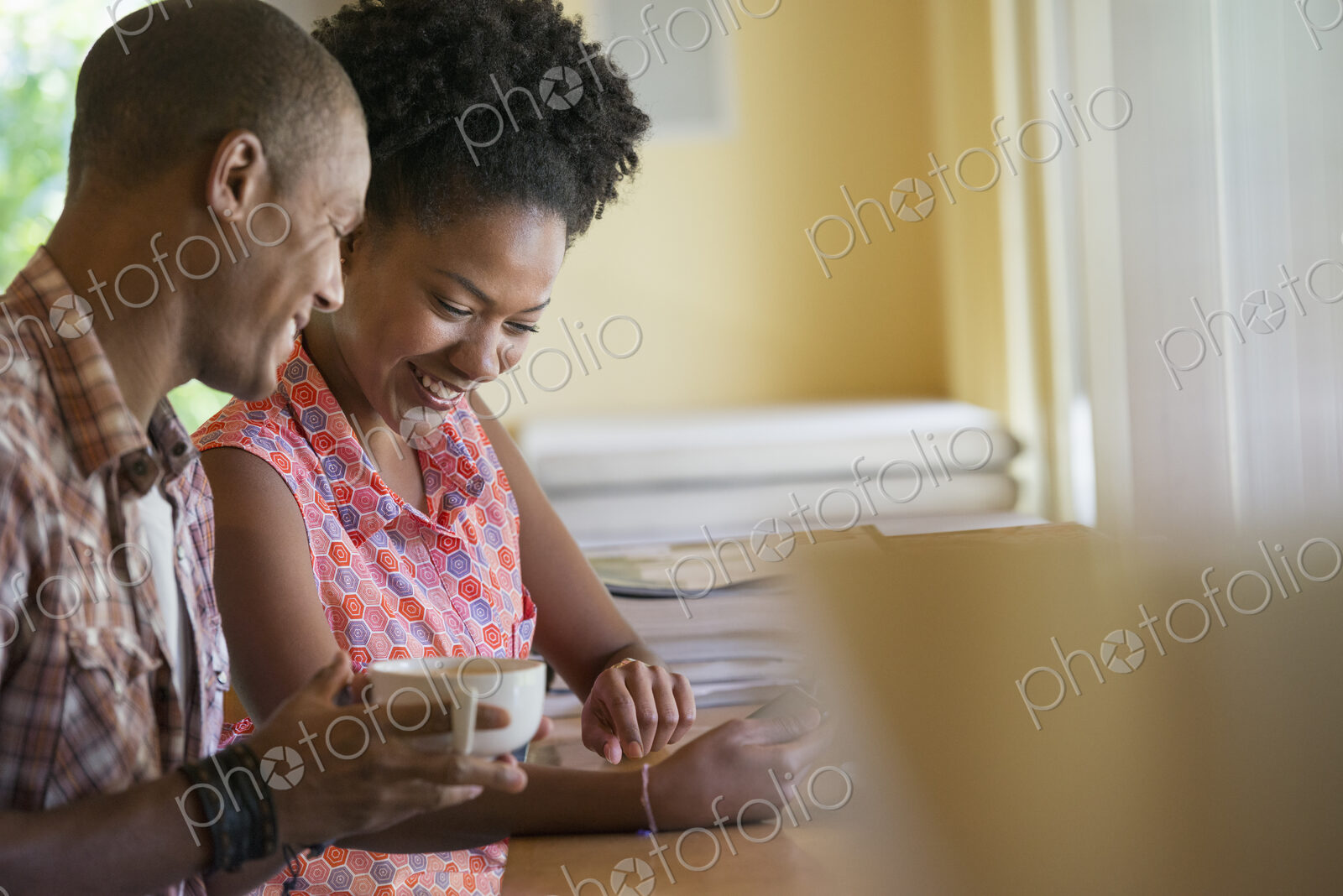 Two people using a digital tablet, seated close together at a cafe. Coffee cups.