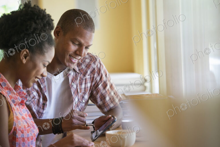 Two people using a digital tablet, seated close together at a cafe. Coffee cups.