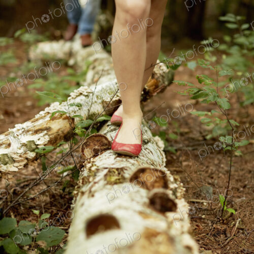 Two people walking along a fallen tree trunk in the woods.