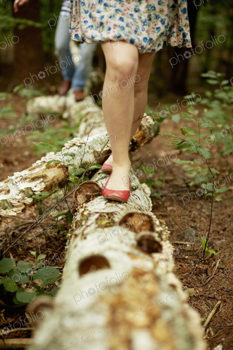 Two people walking along a fallen tree trunk in the woods.