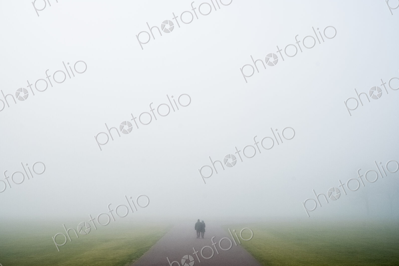 Two people walking along a rural road on a misty day.