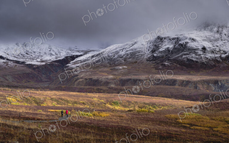 Two people walking towards Denali or Mount McKinley under overcast grey skies.