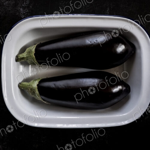 Two purple aubergine egg plant vegetables in an enamel dish. Two purple aubergine egg plant vegetables in an enamel dish.