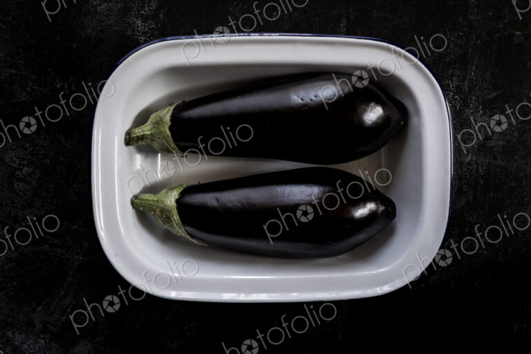 Two purple aubergine egg plant vegetables in an enamel dish.
