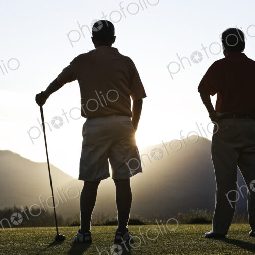 Two senior friends approach the first tee of a golf course at sunrise. Two senior friends approach the first tee of a golf course at sunrise.
