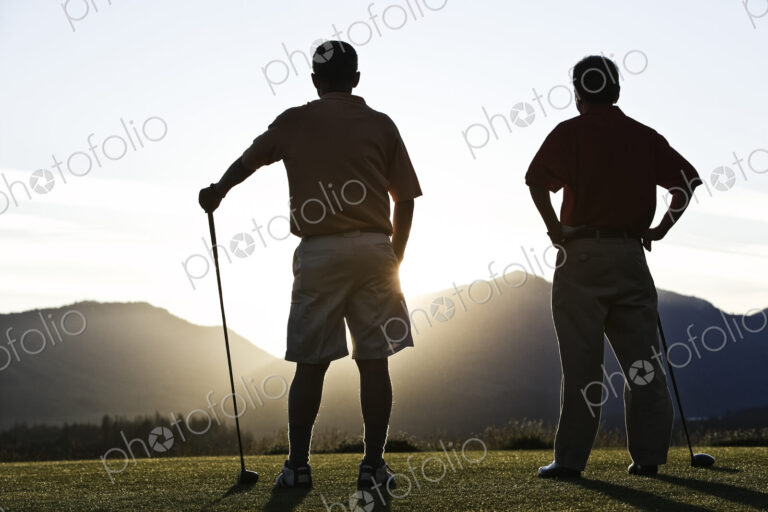 Two senior friends approach the first tee of a golf course at sunrise.