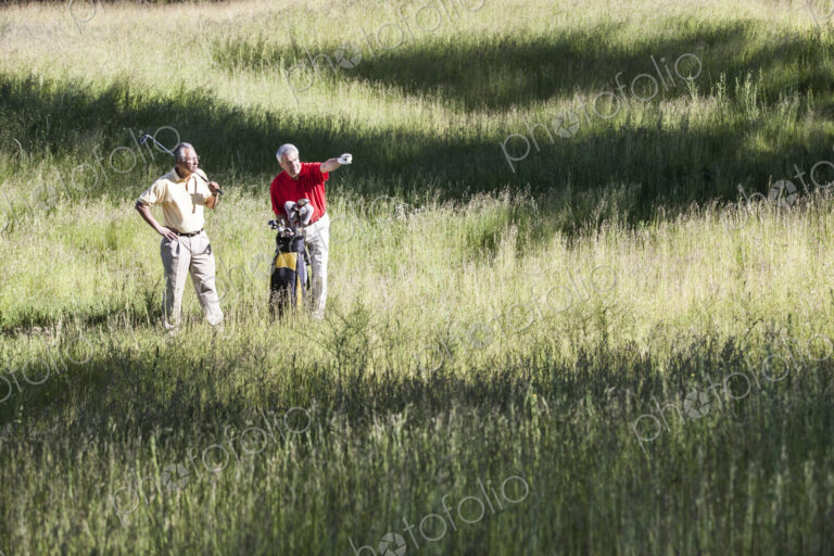 Two senior golfers trying to judge how to play a shot out of heavy rough on a golf course.