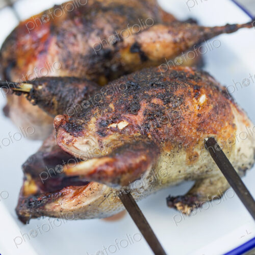 Two small roasted cooked game birds on skewers. Two small roasted cooked game birds on skewers.