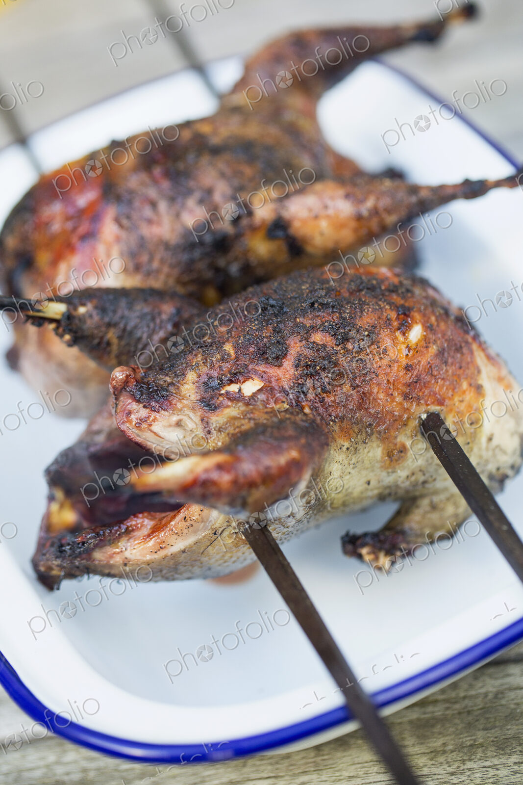 Two small roasted cooked game birds on skewers.