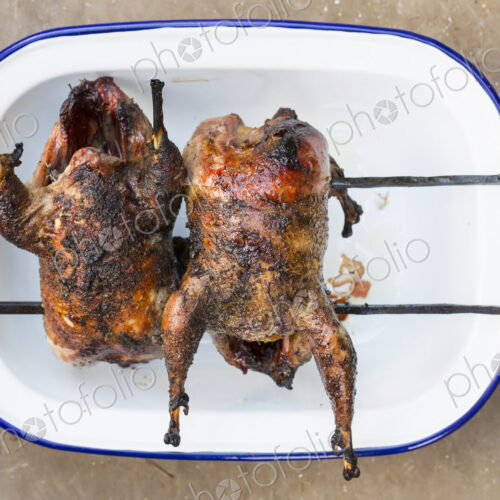 Two small roasted cooked game birds on skewers. Two small roasted cooked game birds on skewers.