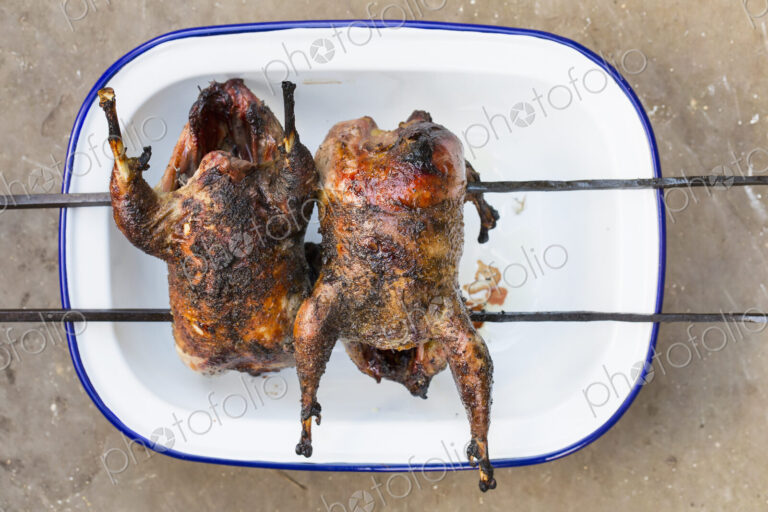 Two small roasted cooked game birds on skewers.