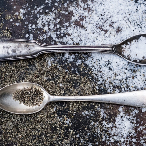Two small spoons with salt crystals on a tabletop.