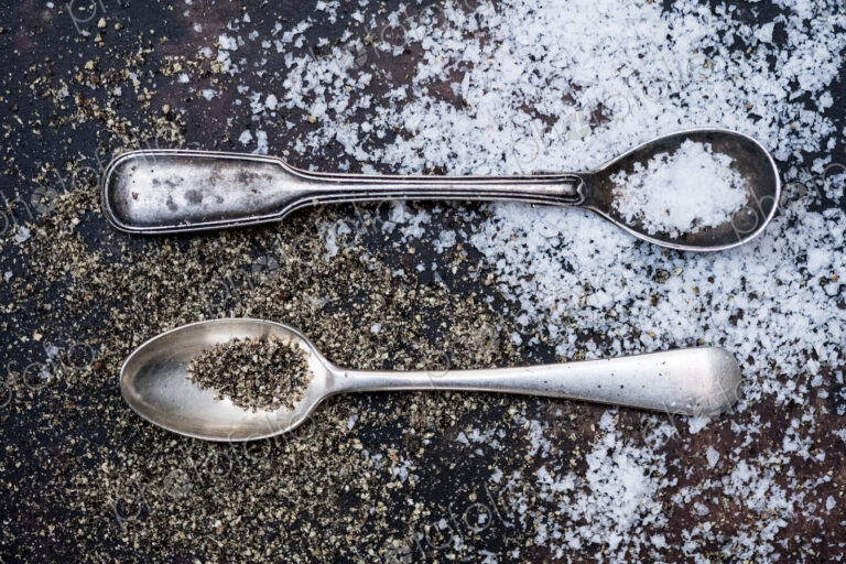 Two small spoons with salt crystals on a tabletop.