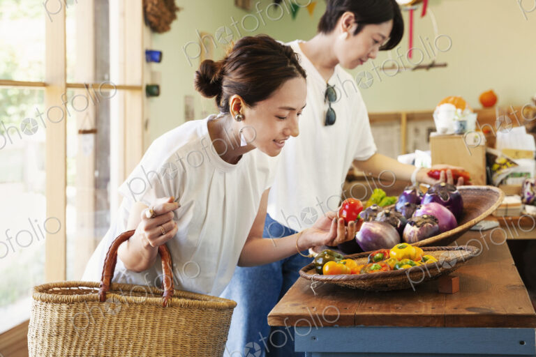 Two smiling Japanese women looking at fresh vegetables in a farm shop.