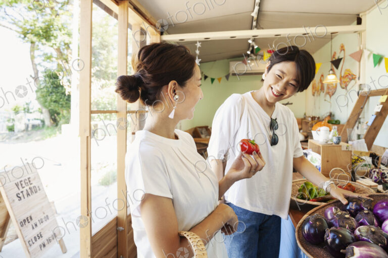 Two smiling Japanese women looking at fresh vegetables in a farm shop.