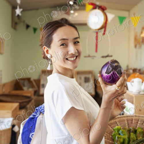 Two smiling Japanese women standing in a farm shop, holding aubergine, looking at camera. Two smiling Japanese women standing in a farm shop, holding aubergine, looking at camera.