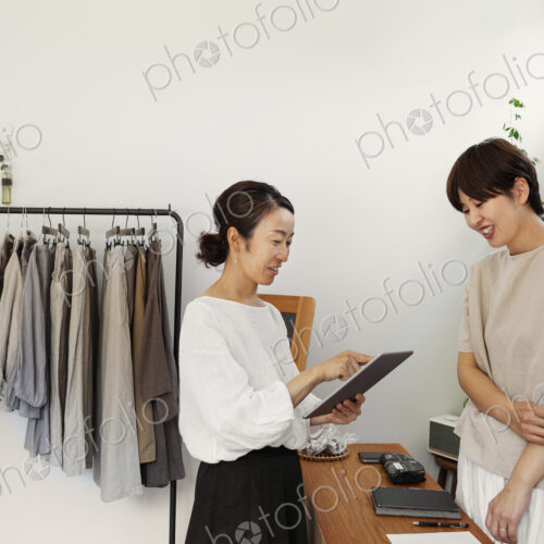 Two smiling Japanese women standing in a small fashion boutique, holding digital tablet. Two smiling Japanese women standing in a small fashion boutique, holding digital tablet.