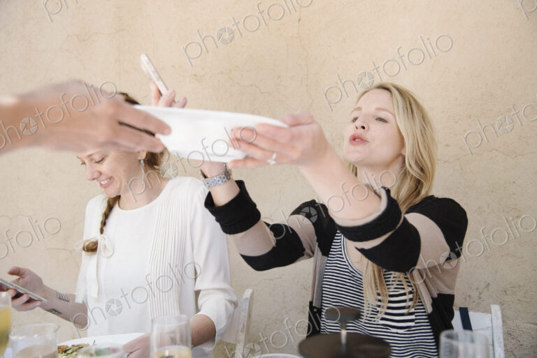 Two smiling women sitting at a table, one reaching for a plate of food.