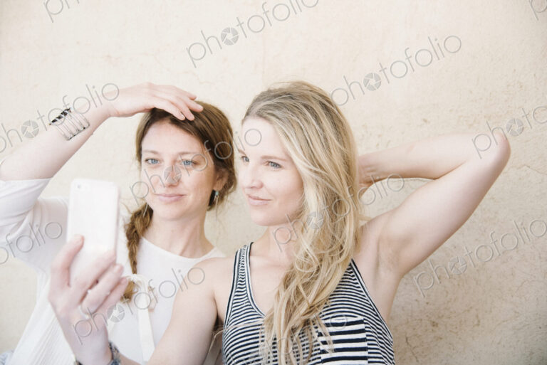 Two smiling women taking a selfie with a cell phone.