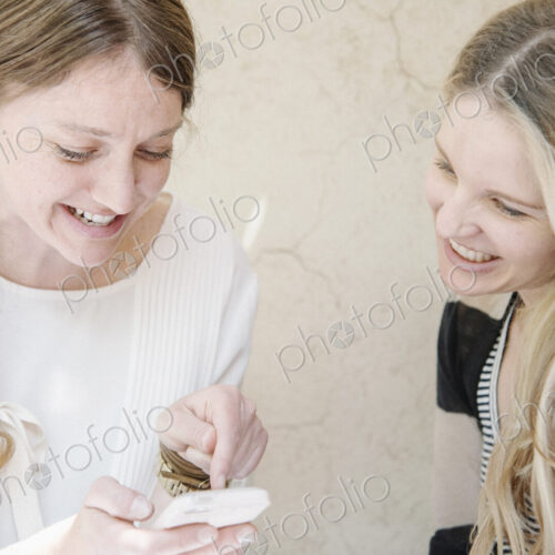Two smiling women with long blond hair sitting at a table, looking at a cell phone. Two smiling women with long blond hair sitting at a table, looking at a cell phone.