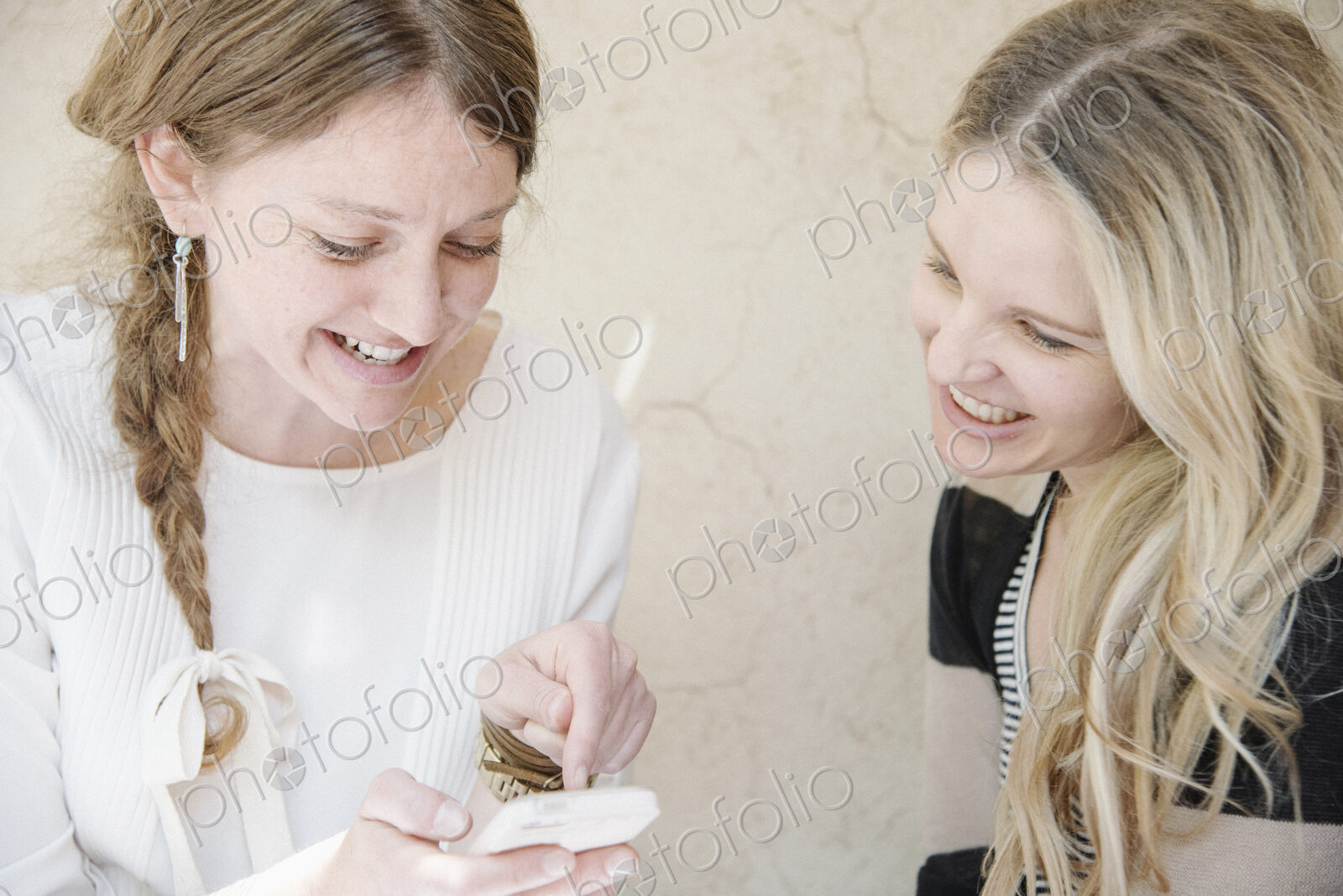Two smiling women with long blond hair sitting at a table, looking at a cell phone.