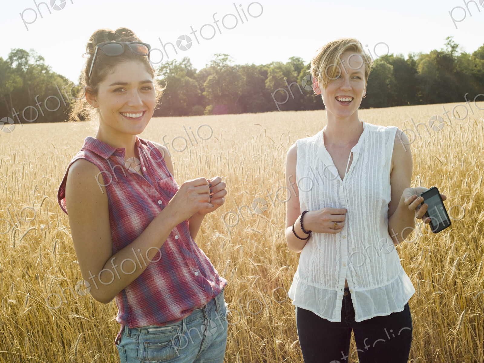 Two smiling young women in a cornfield, one with smart phone.