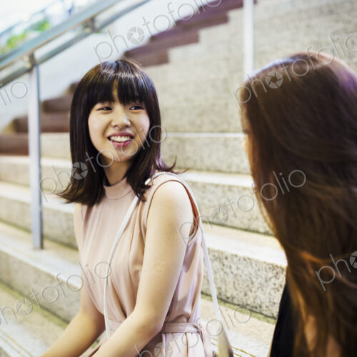 Two smiling young women with long brown hair sitting on a staircase.
