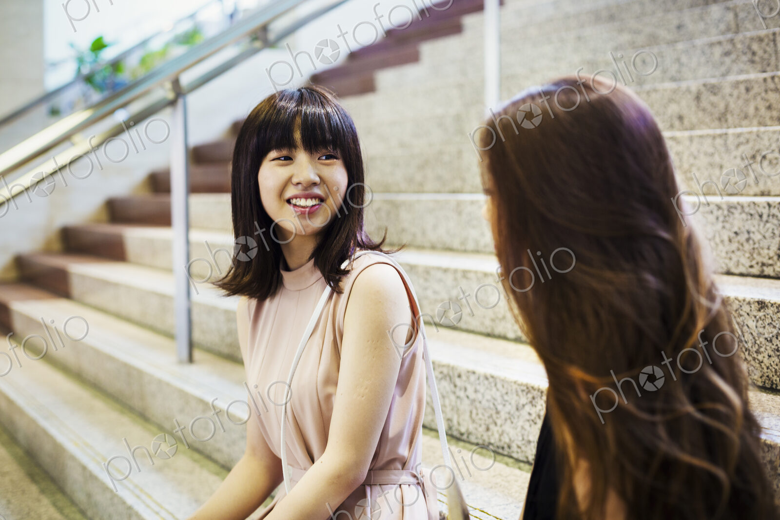 Two smiling young women with long brown hair sitting on a staircase.
