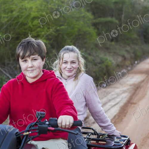 Two teenagers riding on a buggy, all terrain vehicle on a muddy track.
