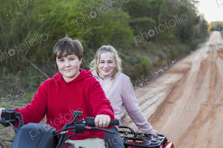 Two teenagers riding on a buggy, all terrain vehicle on a muddy track.