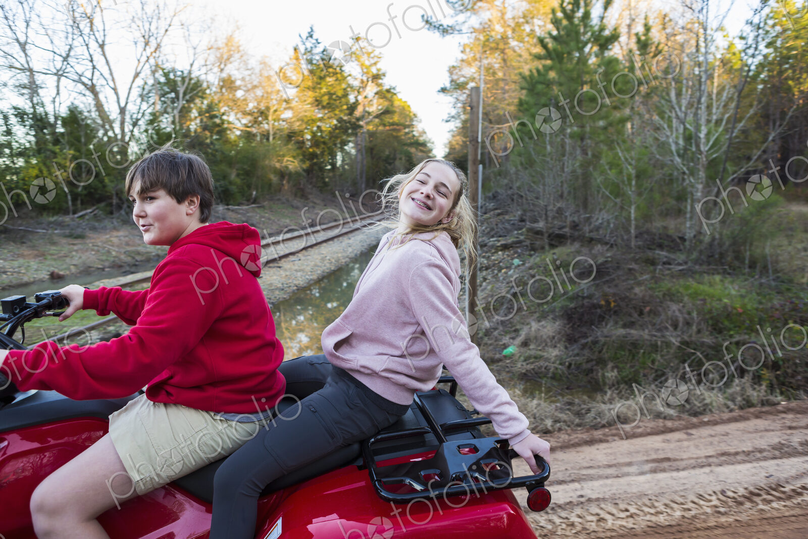 Two teenagers riding on a buggy, all terrain vehicle on a muddy track.