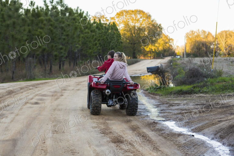 Two teenagers riding on a buggy, all terrain vehicle on a muddy track.