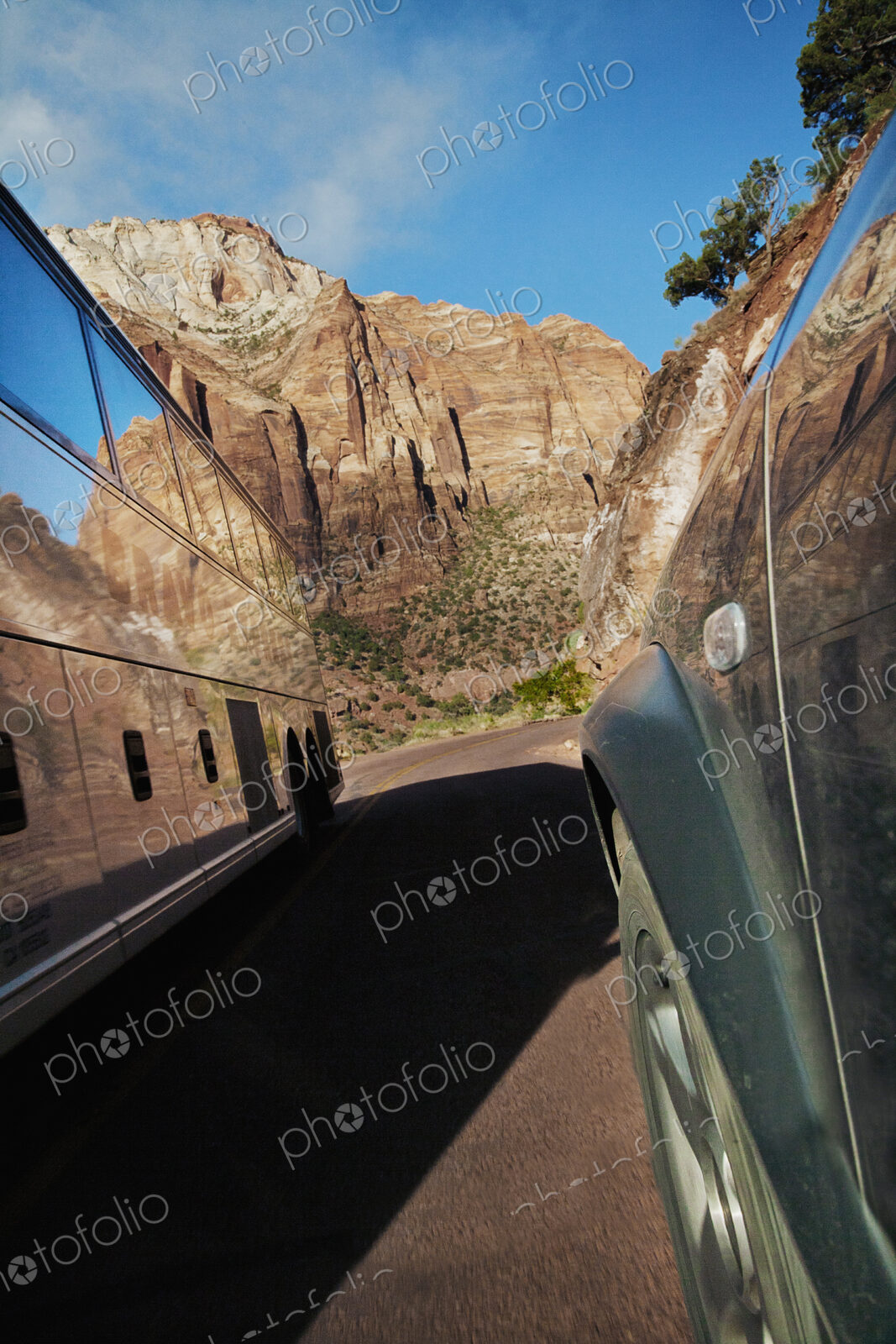 Two vehicle on the road, a public transportation tour bus going through Zion National…