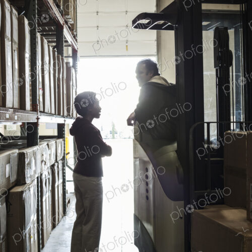 Two warehouse employees talking over an issue while working in a distribution warehouse. Two warehouse employees talking over an issue while working in a distribution warehouse.