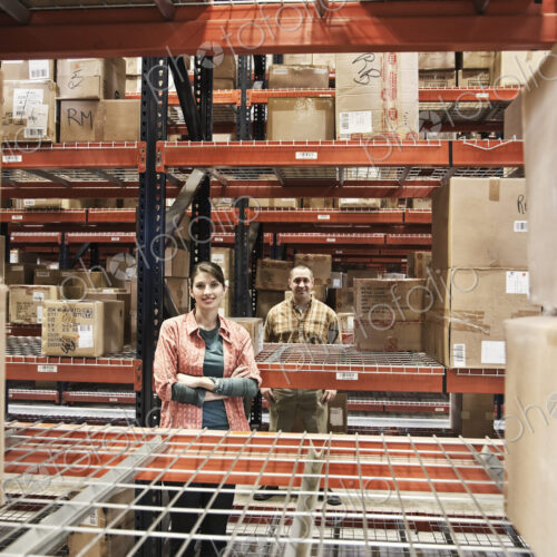 Two warehouse workers among racks of boxed products on racks in a warehouse. Two warehouse workers among racks of boxed products on racks in a warehouse.