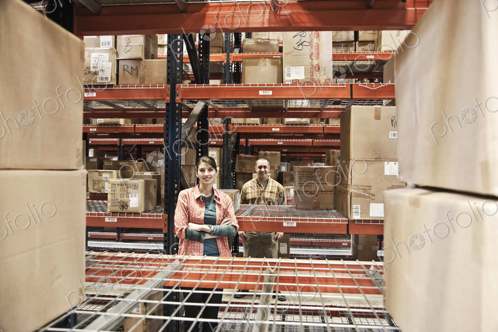 Two warehouse workers among racks of boxed products on racks in a warehouse.