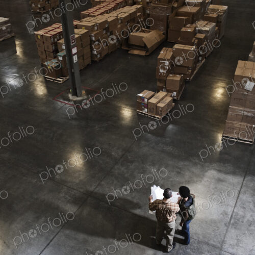 Two warehouse workers going over inventory sheets of products in a distribution warehouse.
